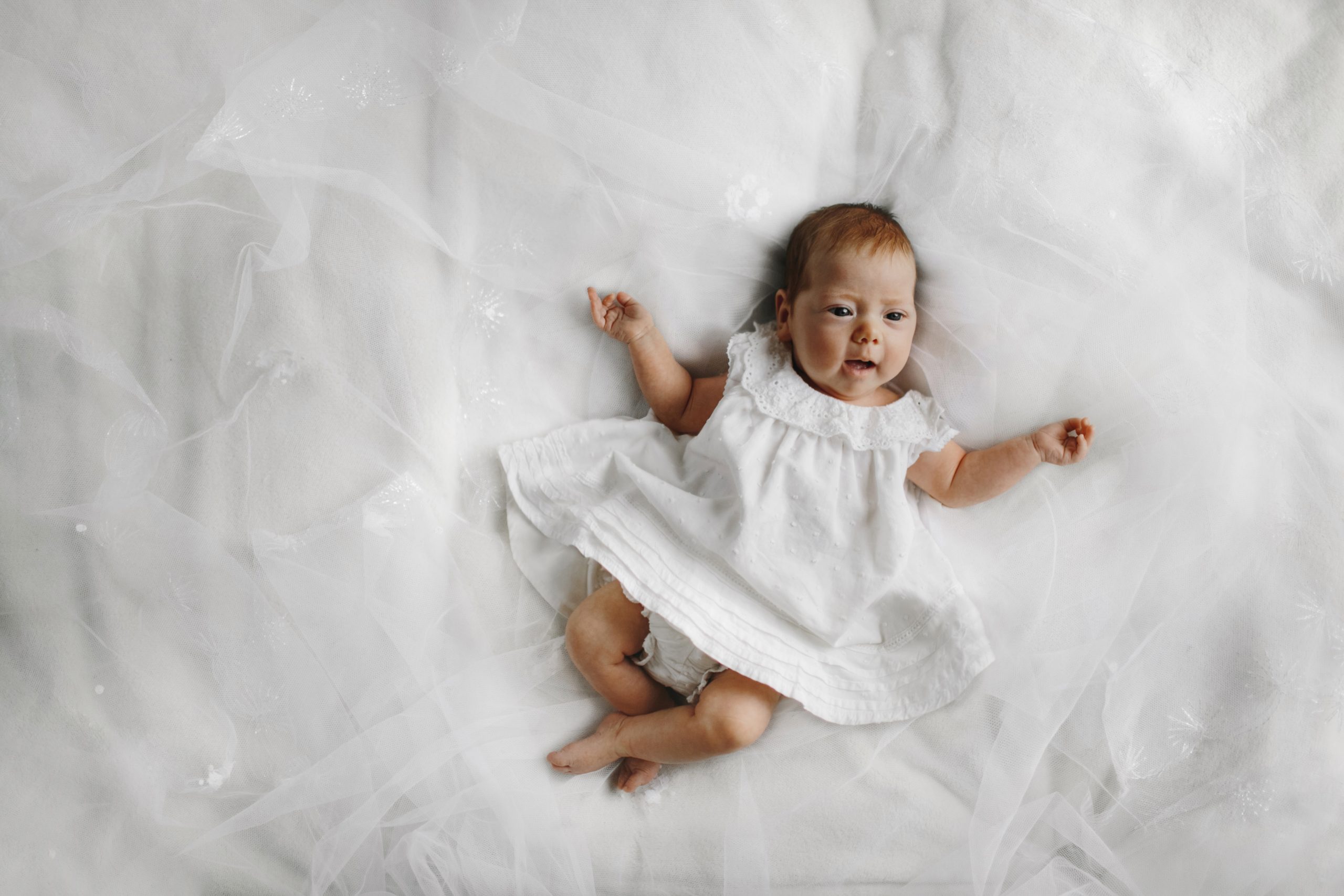 Adorable baby in a white dress lies on a bed